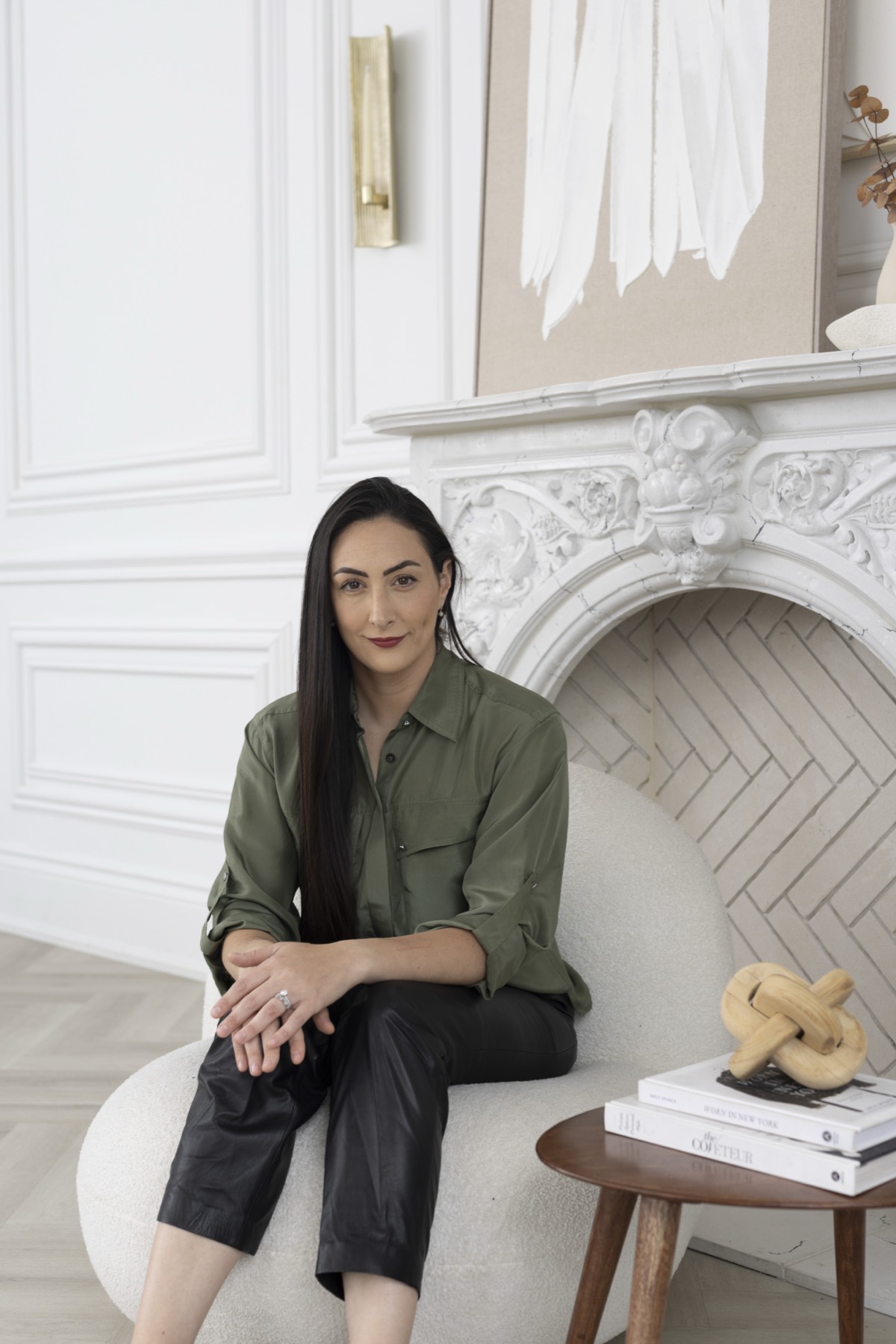 Rebecca Himelfarb seated beside a carved white marble fireplace